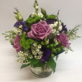 Mixed bouquet of pink roses, purple blooms, and white flowers in a glass vase
