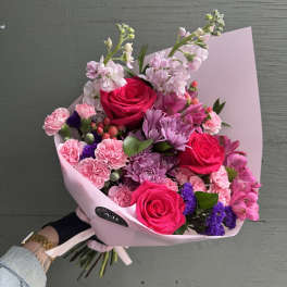 Pink bouquet with roses, carnations, and purple flowers in pastel wrap