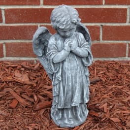 Gray angel statue with folded hands in front of a brick wall