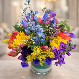 Colorful mixed bouquet in a glass vase with blue, purple, yellow, and pink flowers