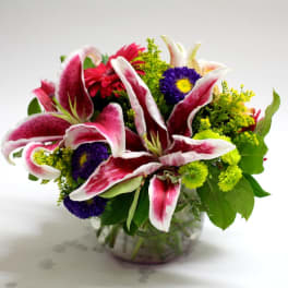 Bouquet of pink-and-white lilies with purple and yellow flowers in a glass vase