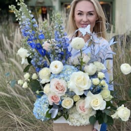 Woman holding a large bouquet of white, pink, and blue flowers in a box