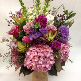 Mixed bouquet of pink, purple, and white flowers in a burlap-wrapped vase