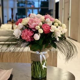 Pink and white peonies in a glass vase with a ribbon wrap