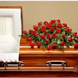 Red rose spray on a wooden casket beside a white draped panel