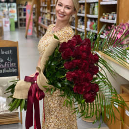 Woman holding a large bouquet of red roses wrapped in burlap with a burgundy ribbon