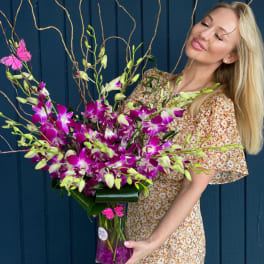 Woman holding a large bouquet of purple and white orchids in a glass vase