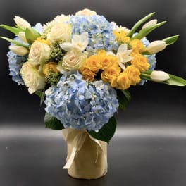 Blue hydrangeas with yellow and white roses in a wrapped vase arrangement