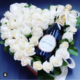 White roses arranged around a champagne bottle with a white ribbon