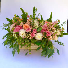 Pink and peach roses in a low wooden container with greenery