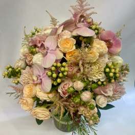 Bouquet of pale pink orchids, cream roses, and green berries in a glass vase