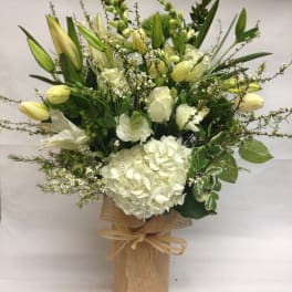 White floral arrangement with lilies and hydrangea in a burlap-wrapped vase