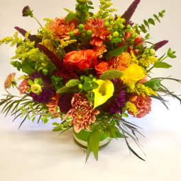 Bright mixed bouquet in a glass vase with orange, yellow, and purple flowers