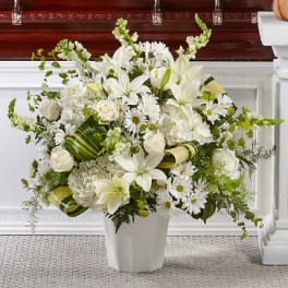 White floral arrangement in a white vase with lilies, roses, and daisies