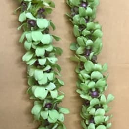 A green floral lei with small purple accents laid on a plain surface