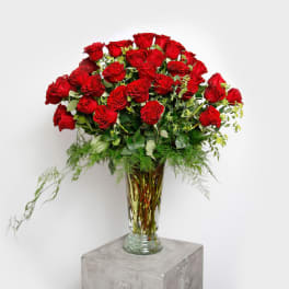 Tall vase arrangement of red roses with greenery