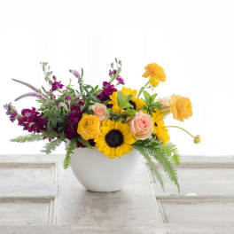 Mixed bouquet in a white vase with sunflowers, roses, and orange blooms
