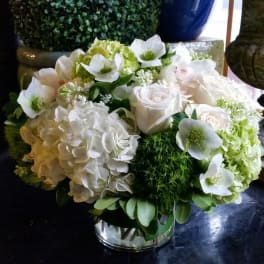White floral arrangement in a clear glass vase with hydrangeas and roses