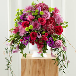 Large pink and purple floral arrangement in a white pedestal vase