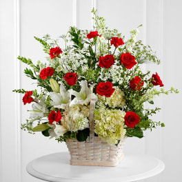 Basket arrangement of red roses, white lilies, and pale hydrangeas
