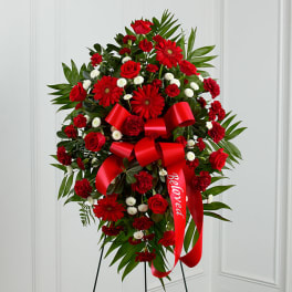 Red roses and gerbera daisies in a standing spray with a red ribbon