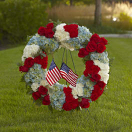 Floral wreath of red roses, white carnations, and blue hydrangeas with small American flags