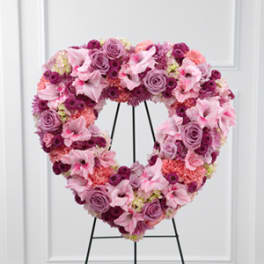 Heart-shaped floral wreath in pink and purple tones on a black stand
