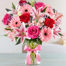 Pink and red bouquet of roses, lilies, and gerbera daisies in a glass vase