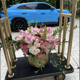 Pink and white floral arrangement in a gold vase on a cart