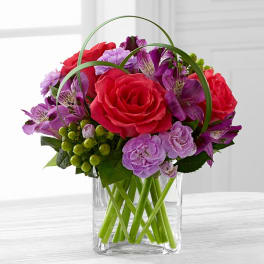 Bouquet of red roses and purple flowers in a clear glass vase