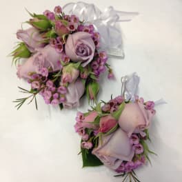 Two lavender rose corsages with pink filler flowers and white ribbon