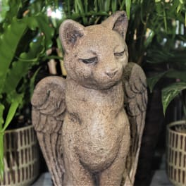 Stone cat statue in front of potted green plants