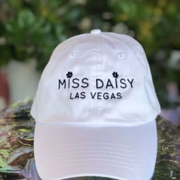 White baseball cap embroidered with "MISS DAISY LAS VEGAS"