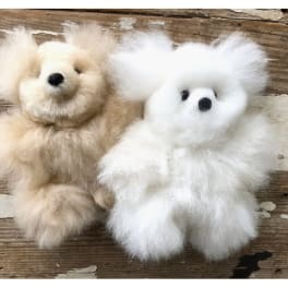 Two fluffy teddy bears, one beige and one white, on a wooden surface.