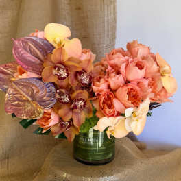 Peach roses and orchids arranged in a green glass vase
