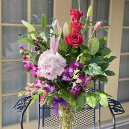 Bouquet of red roses, pink lilies, and orchids in a clear glass vase
