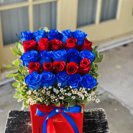 Red and blue roses arranged in a red box with a ribbon