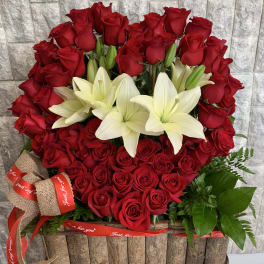 Red roses and white lilies arranged in a rustic basket with ribbon