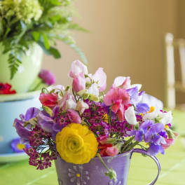 Colorful mixed flower arrangement in a purple metal teacup planter