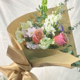 Hand-tied bouquet of pink roses, white blooms, and eucalyptus wrapped in brown paper