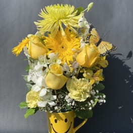 Yellow flower bouquet in a smiley-face mug with butterfly accents