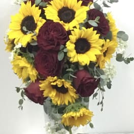 Bouquet of yellow sunflowers and burgundy roses in a clear vase
