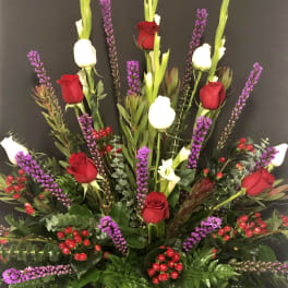 Tall arrangement of red and white roses with purple spikes in a decorative vase