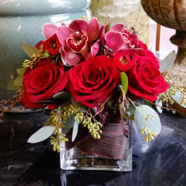 Red roses and pink orchids in a square glass vase
