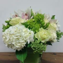 White and green floral arrangement in a square glass vase