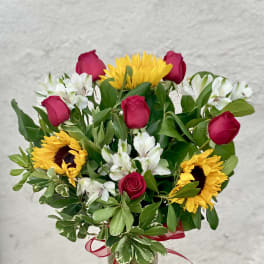 Bouquet of red roses, sunflowers, and white alstroemeria in a glass vase