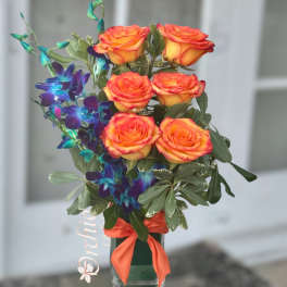 Orange roses with blue orchids in a glass vase