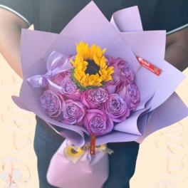Bouquet of purple roses with a yellow sunflower center wrapped in lavender paper