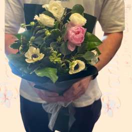 Handheld bouquet of white and pink flowers wrapped in dark paper