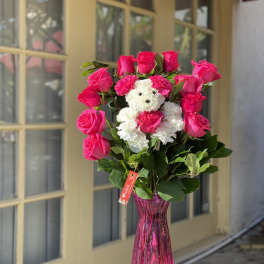 Pink roses arranged around a small white teddy bear in a pink vase